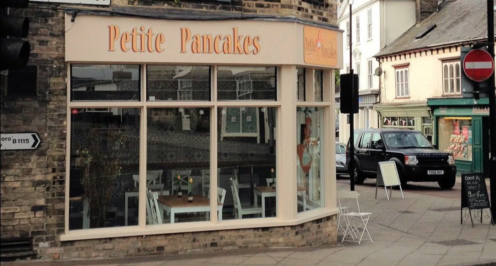 Cozy pancake shop on a street corner with large glass windows and outdoor seating.