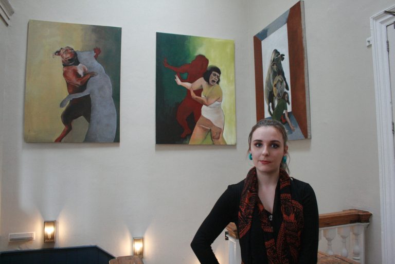 Woman standing in art gallery with colourful paintings on the wall.