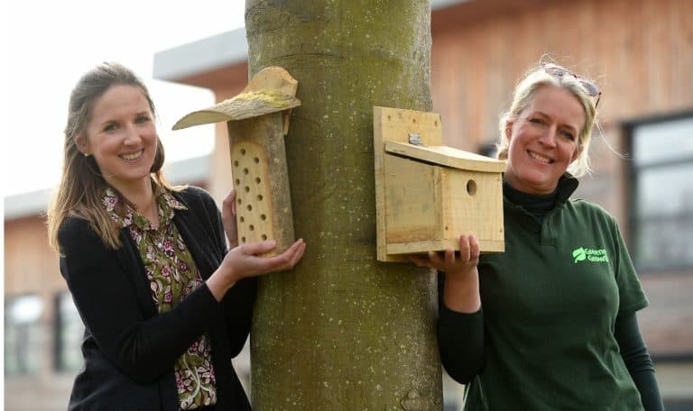 A woman and a girl holding birdhouses on a tree for conservation in Suffolk.