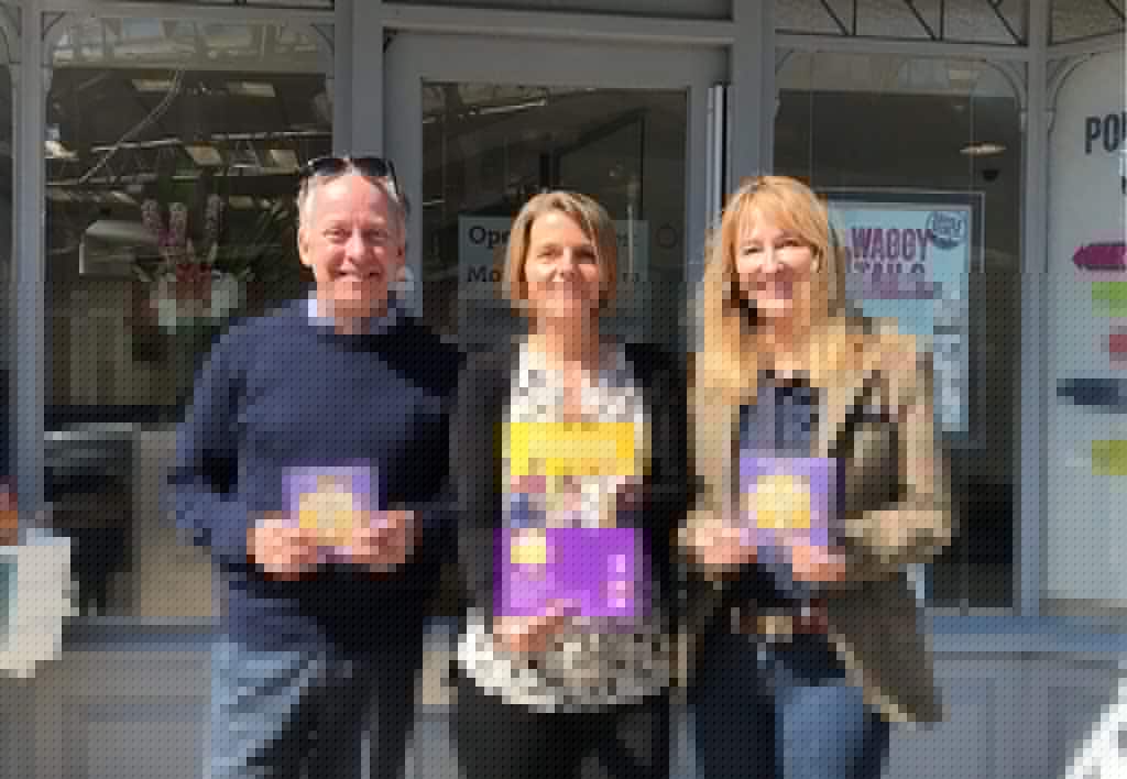 Three professionals holding promotional materials outside Suffolk Business office.