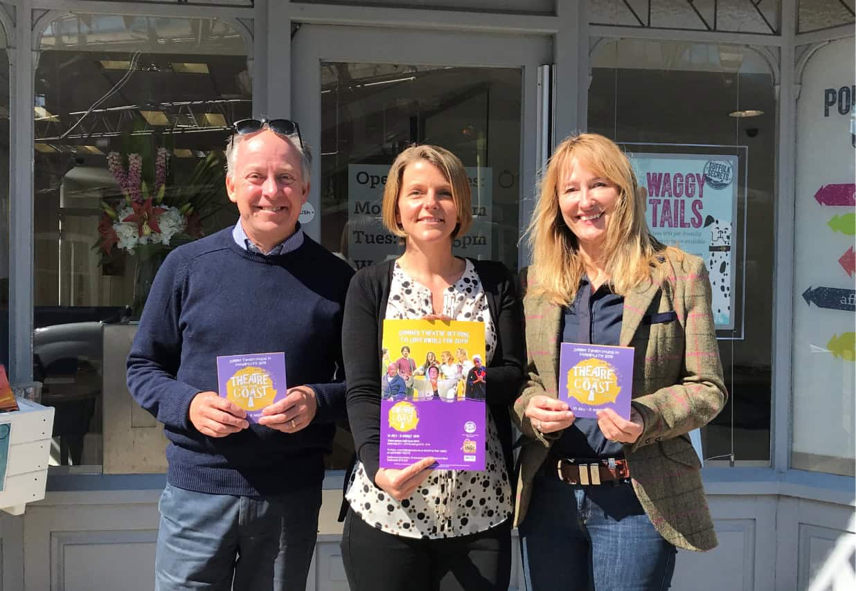 Three professionals holding promotional materials outside Suffolk Business office.