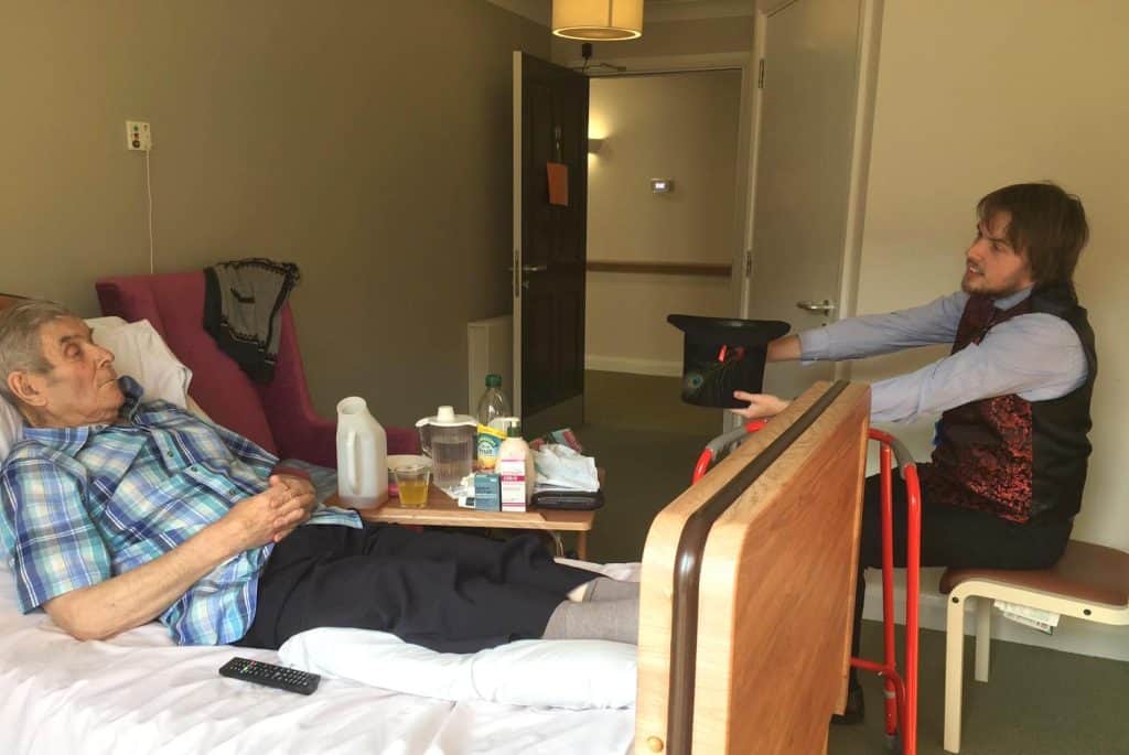 Elderly man in hospital bed receiving care from a young caregiver in a healthcare setting.