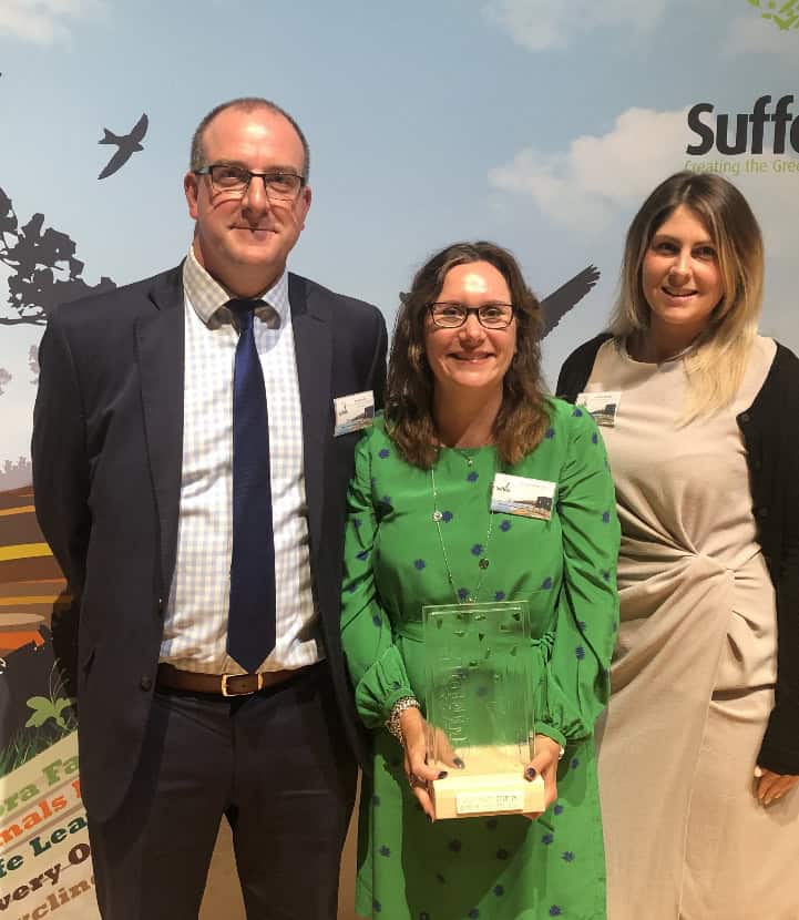 Three professionals at Suffolk Business event, celebrating success and networking.
