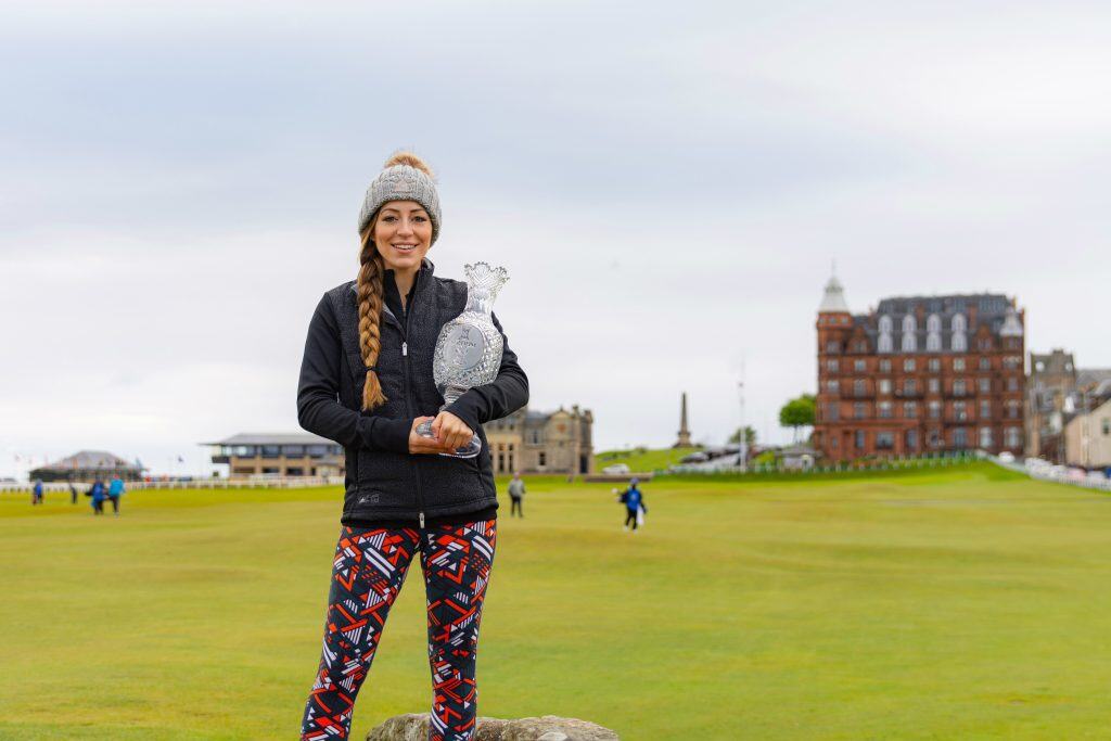 Woman in Suffolk holding a trophy on the golf course, smiling and dressed warmly.