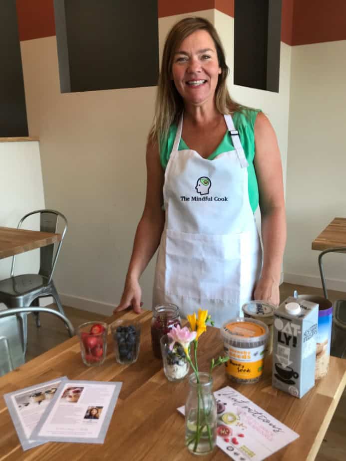 Healthy cooking demonstration with a woman in an apron showcasing fresh ingredients.