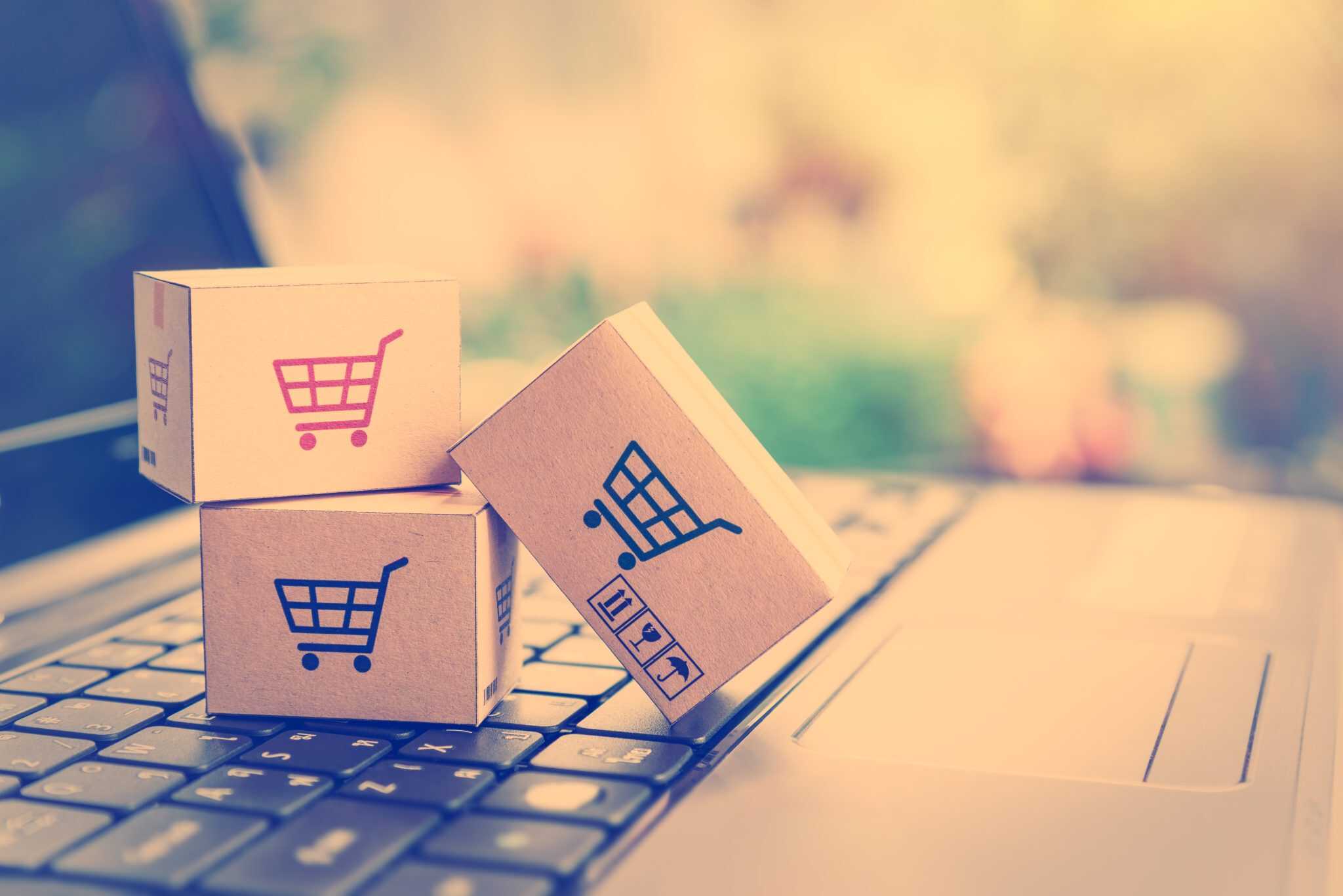 Online shopping concept with cardboard boxes featuring shopping cart icons on a laptop keyboard.