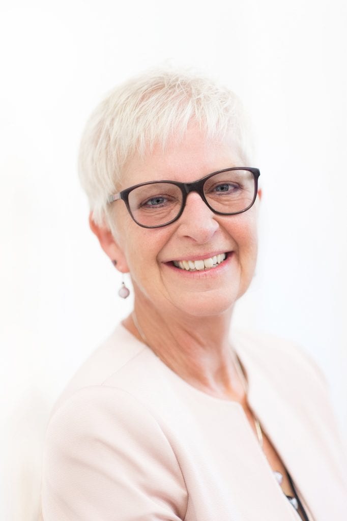 Businesswoman with short white hair and glasses smiling for Suffolk Business branding.