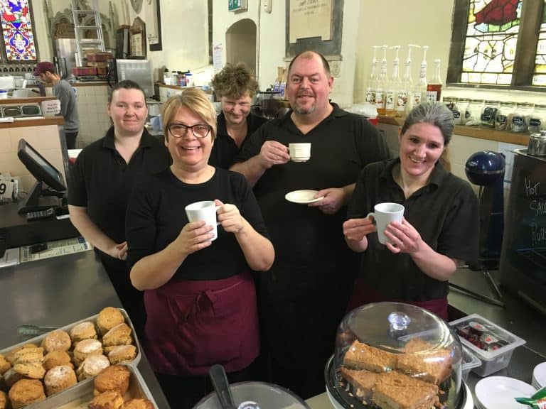 Suffolk Business team members smiling and enjoying coffee in a café setting.