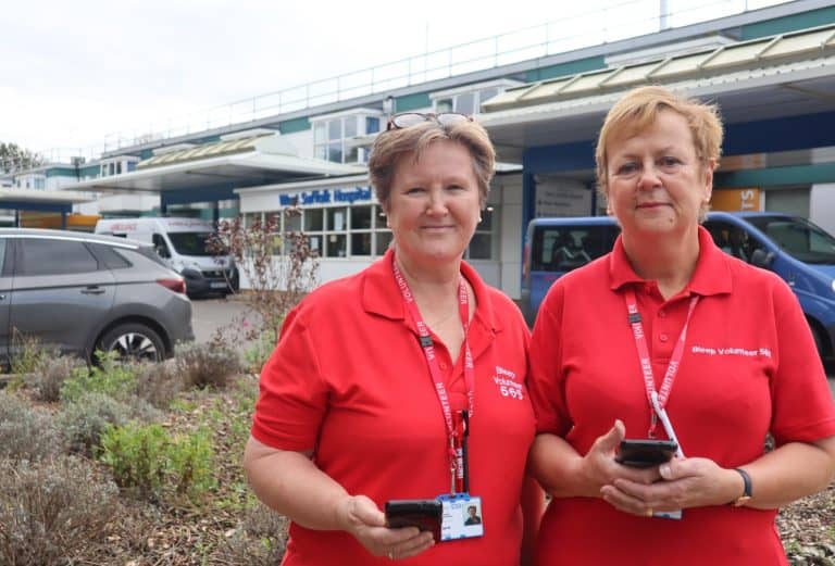 Two women in red Suffolk Business volunteer uniforms outside hospital entrance.