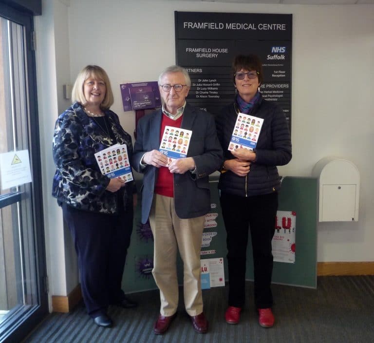 Medical centre staff team in Suffolk holding health information leaflets.