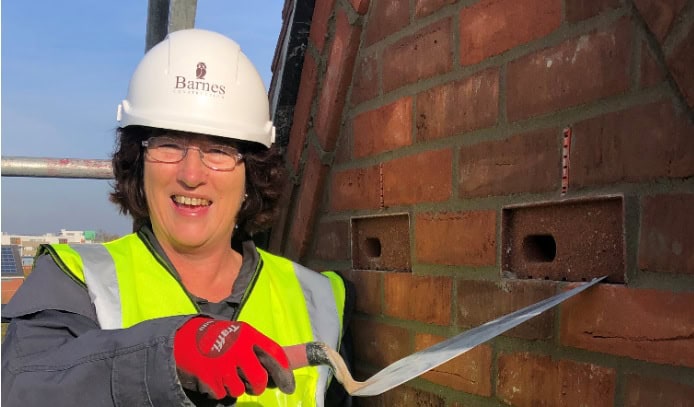 Construction worker inspecting brick wall with trowel, wearing safety gear.