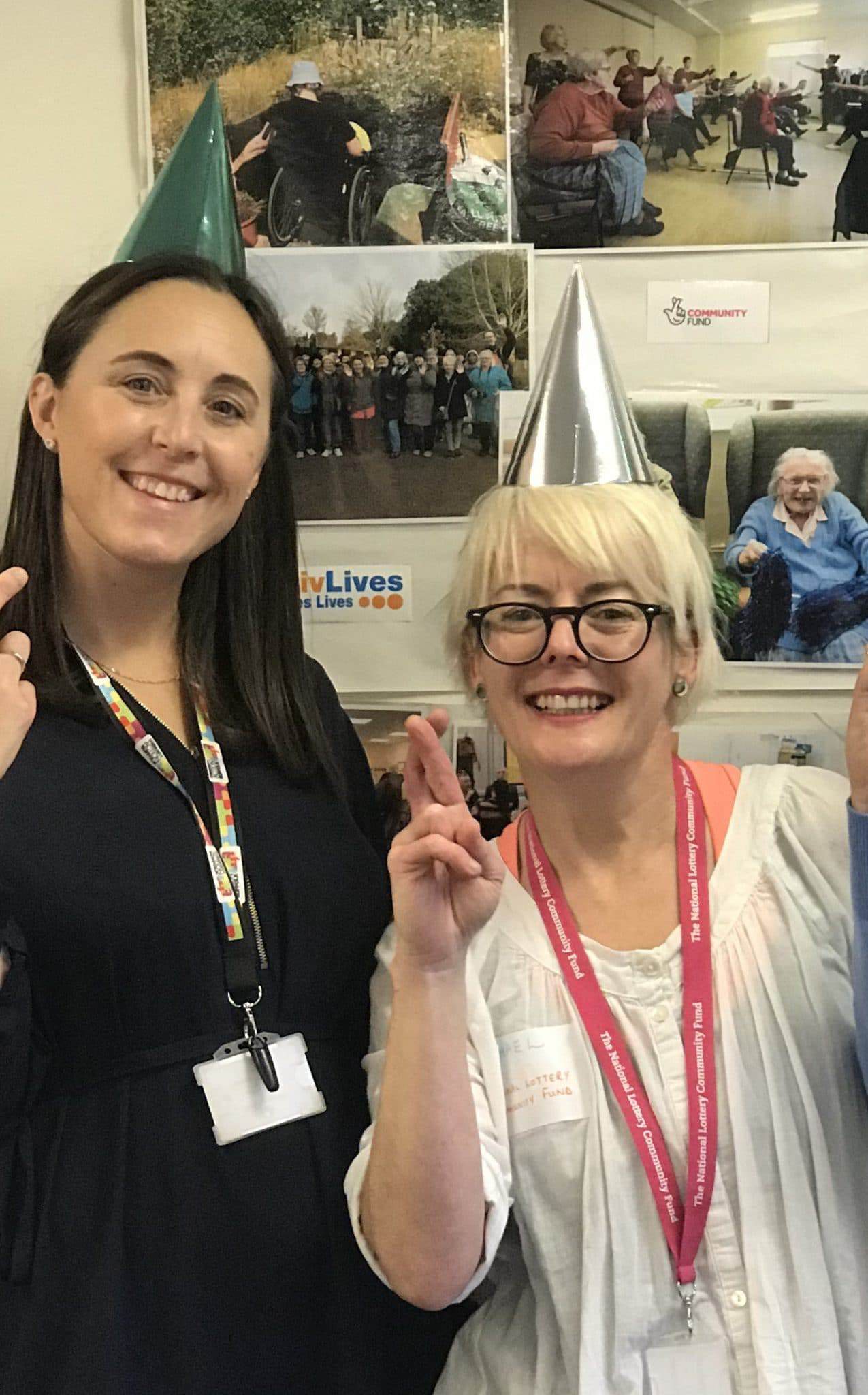 Two women celebrating at Suffolk community event, wearing party hats and smiling.