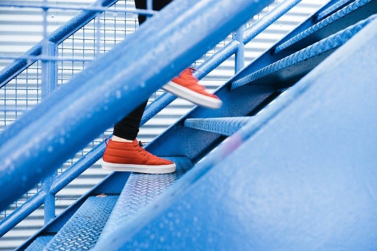 Modern office staircase with blue metal stairs and a person wearing red sneakers.