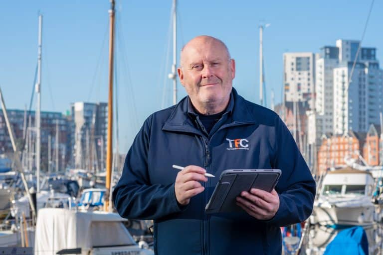 Maritime professional using tablet at a marina with modern buildings in the background.