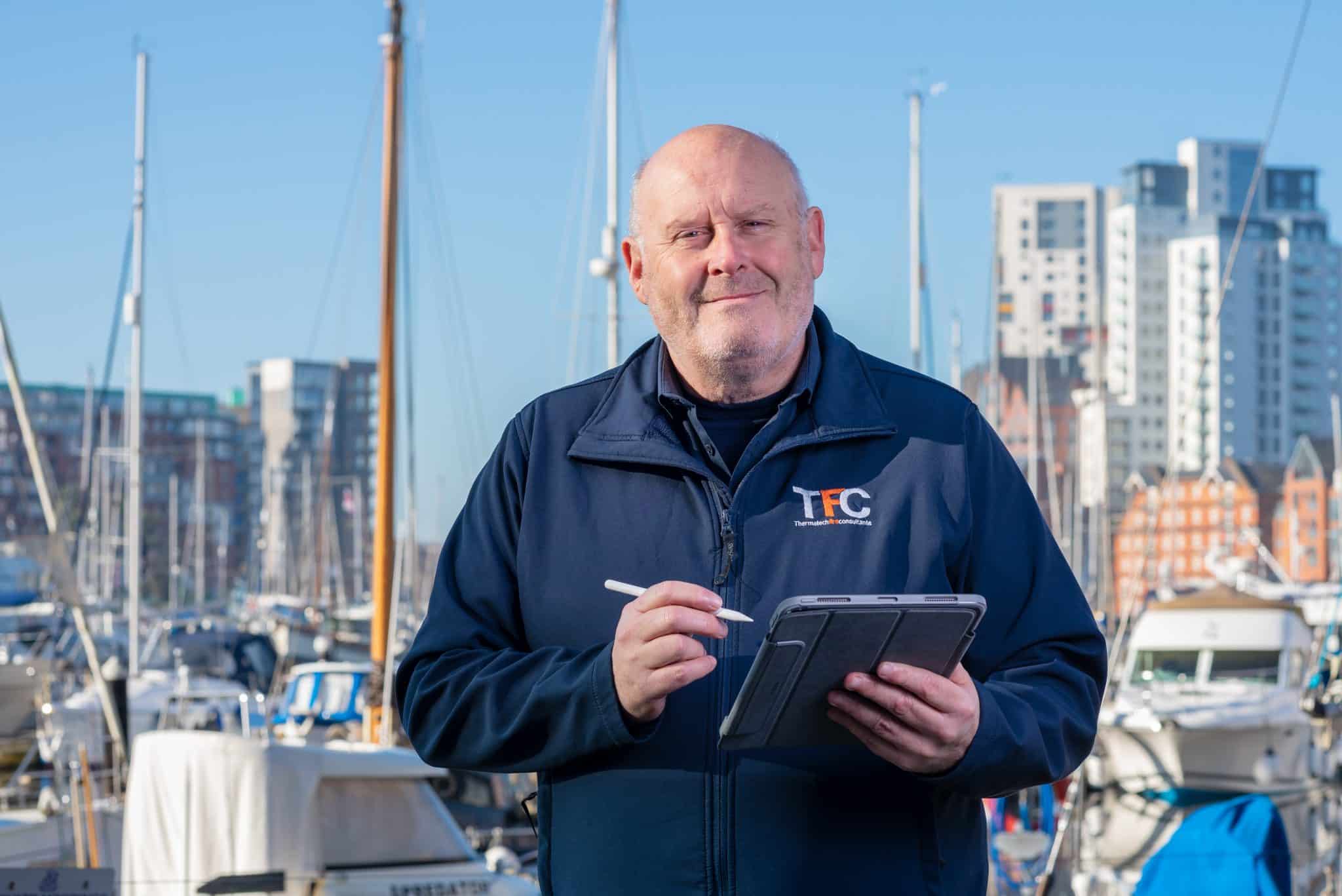 Maritime professional using tablet at a marina with modern buildings in the background.