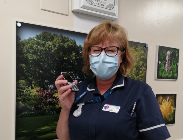 Healthcare worker with face mask holding a phone in a medical setting.