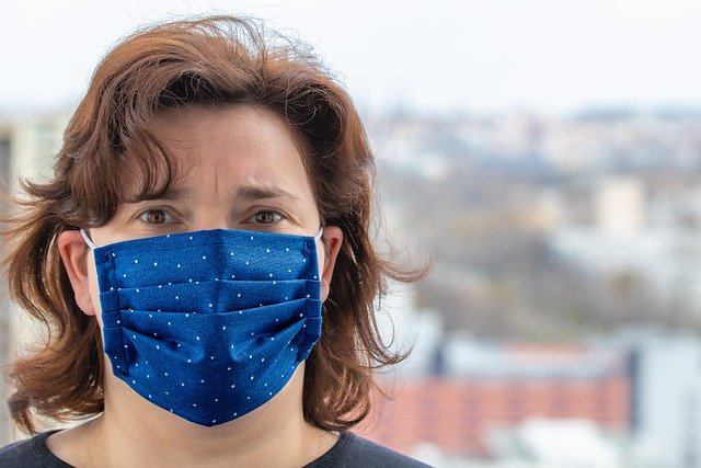 Woman wearing a blue protective face mask outdoors in an urban environment.