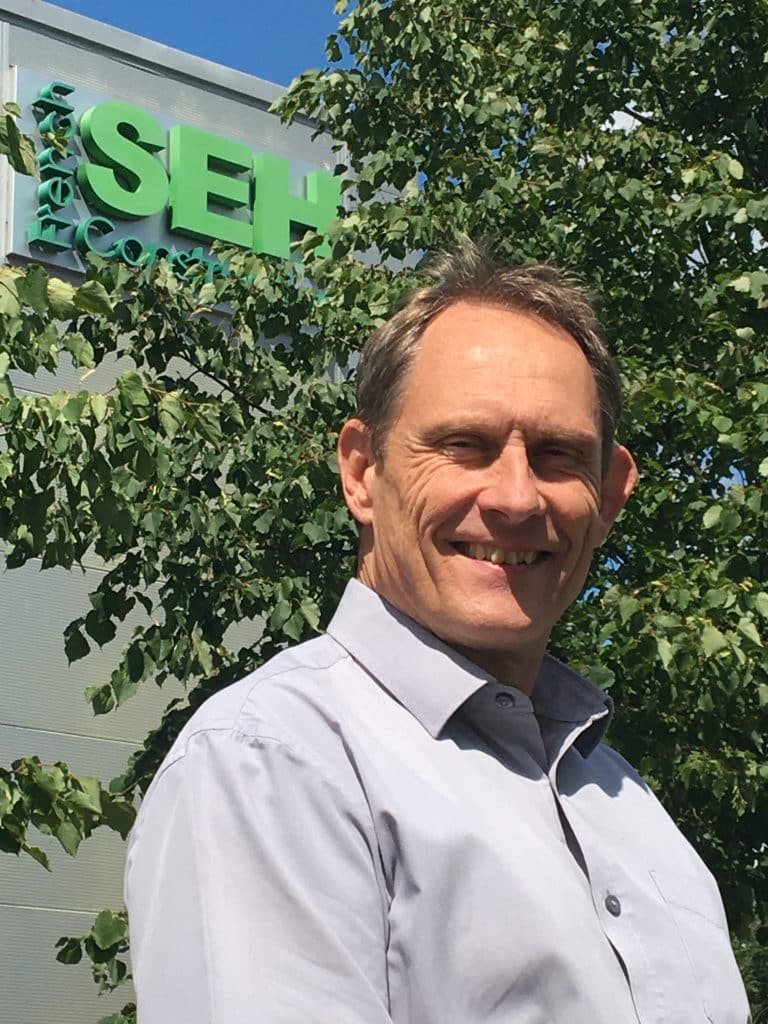 Suffolk Business professional outdoors near office building with greenery.