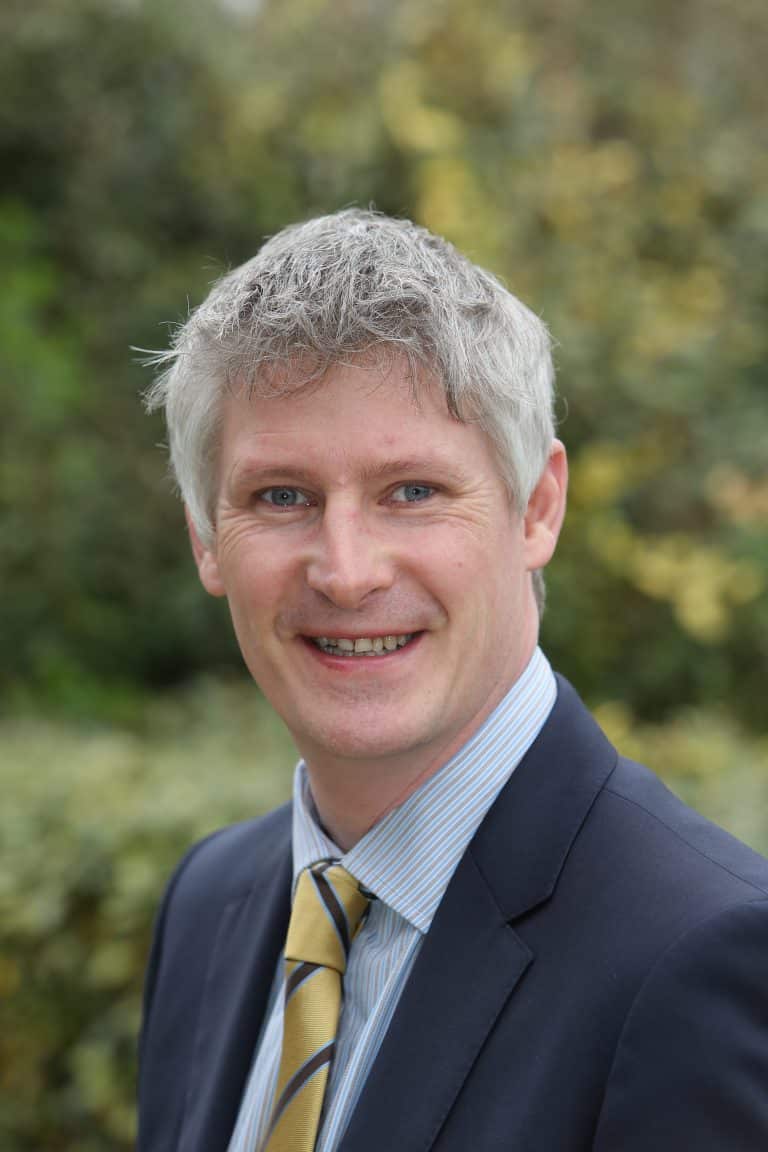 Business professional smiling outdoors in Suffolk, dressed in a suit and tie.