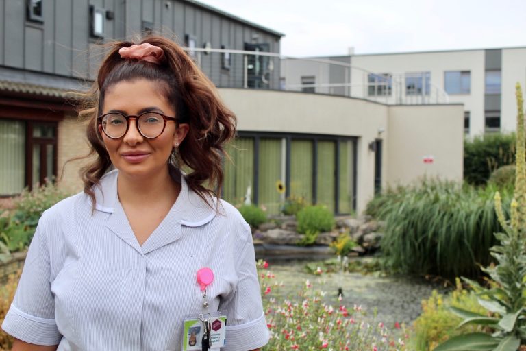 Healthcare professional wearing scrubs and glasses outdoors in Suffolk.