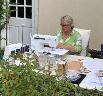 A woman working on a sewing machine outdoors in a garden setting.