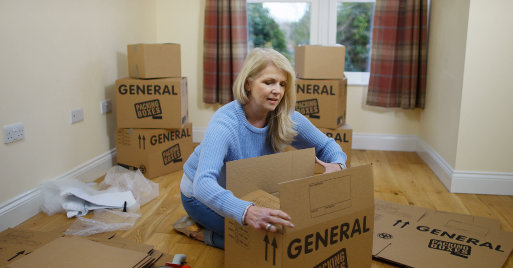 Woman packing boxes for moving house in a bright room, preparing for relocation.