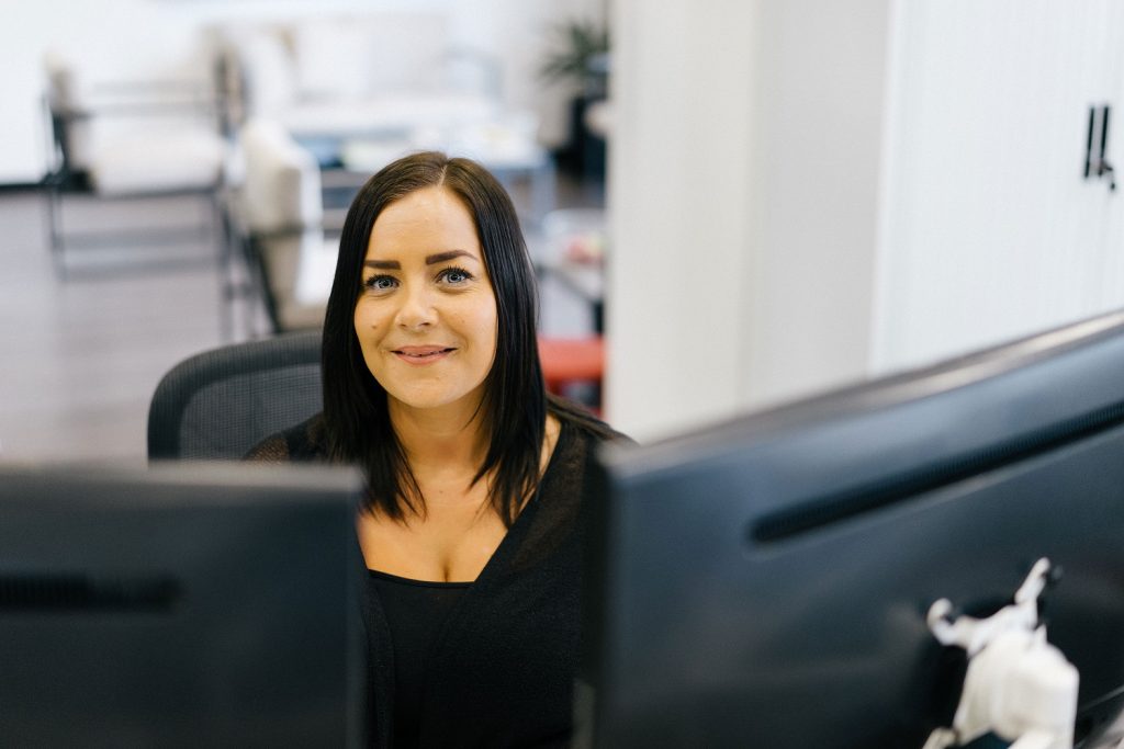 Office professional working at desk in Suffolk business environment, smiling at camera, with compute.