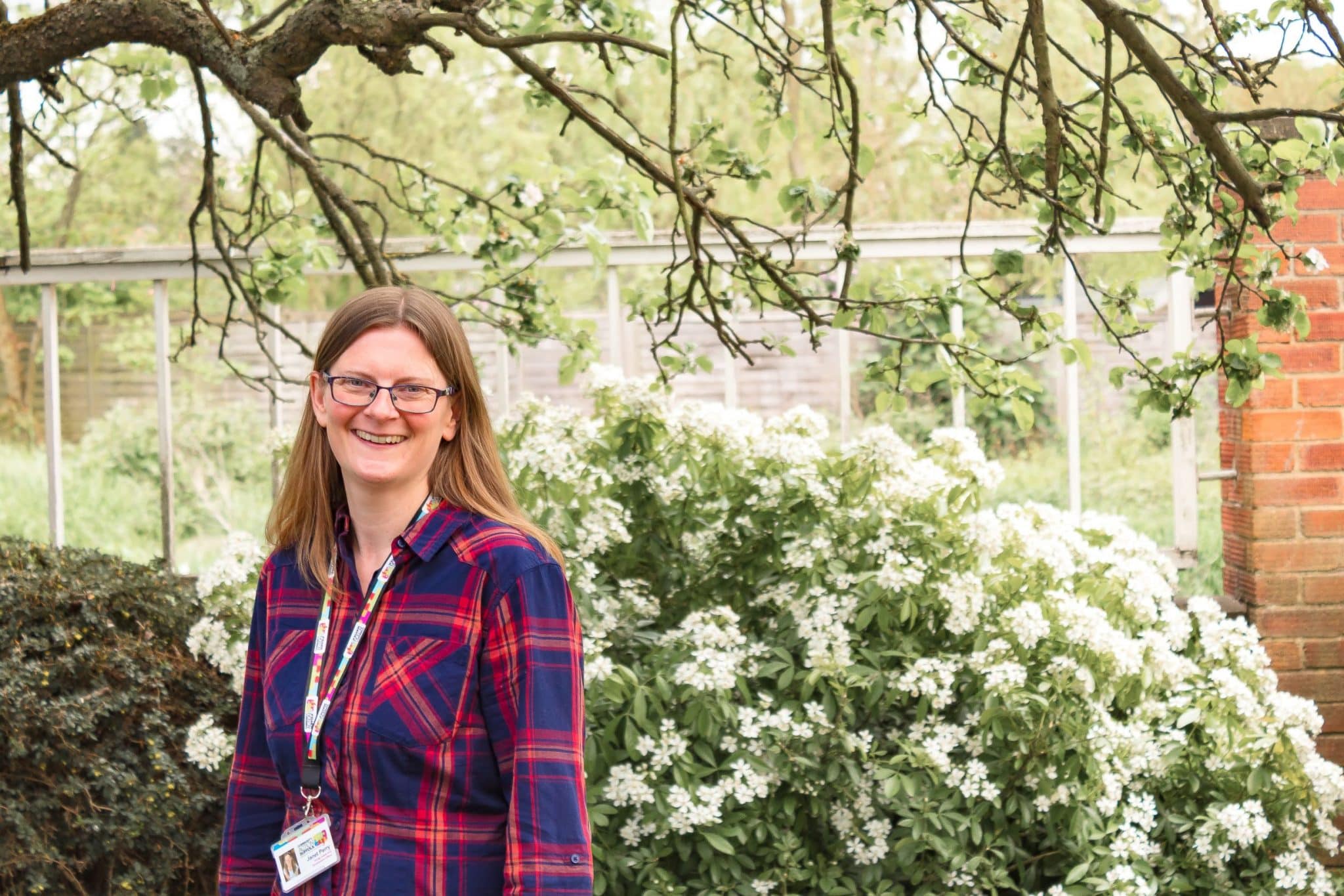 Suffolk businesswoman Janet Perry smiling outdoors in a garden with white flowering bushes and trees.