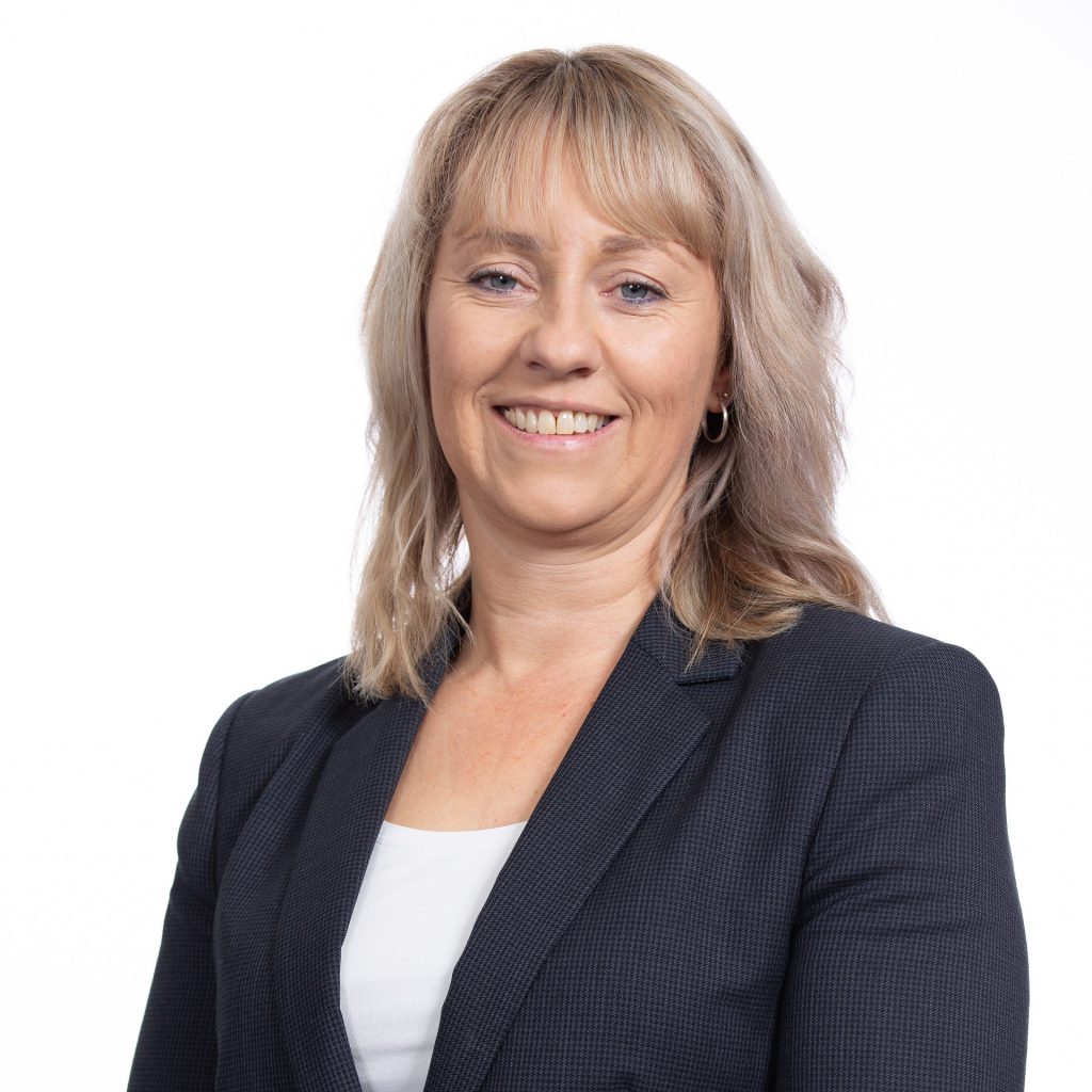 Professional businesswoman smiling in a dark blazer and white top, representing Suffolk Business and.