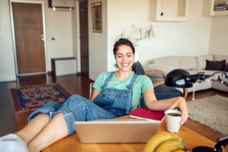 Remote work woman with laptop, coffee, and headphones in cozy living room.