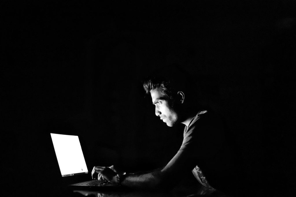 Young man working on a laptop in a dark room, representing Suffolk business innovation.