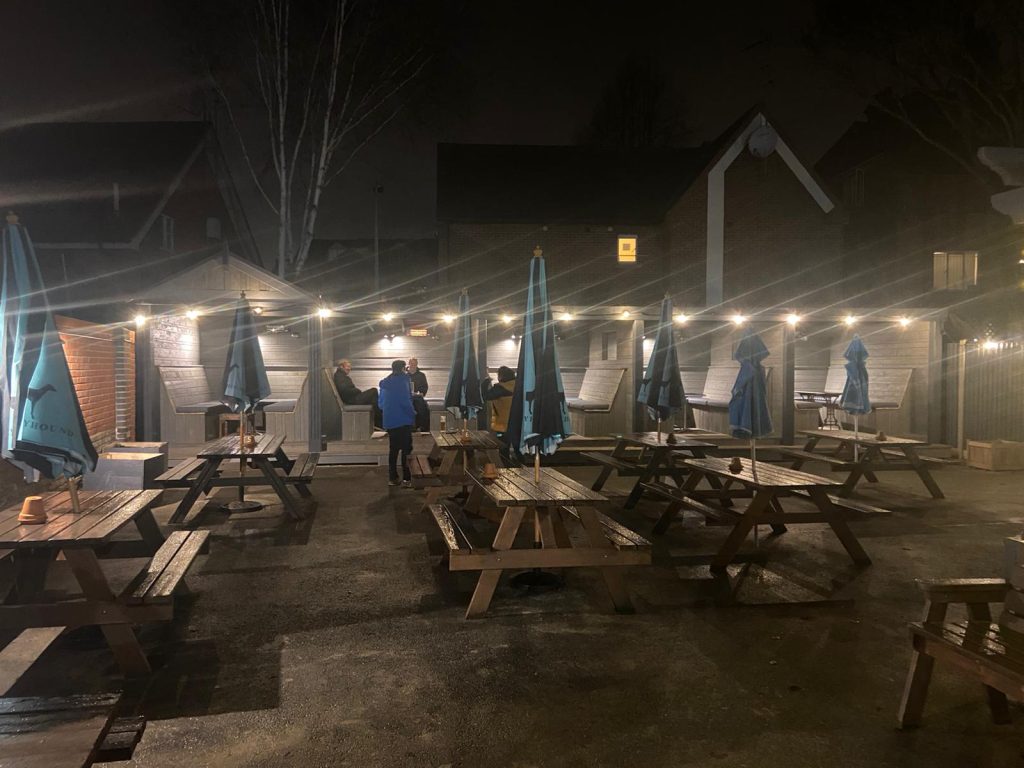 Outdoor dining area with wooden picnic tables and string lights in Suffolk, UK.