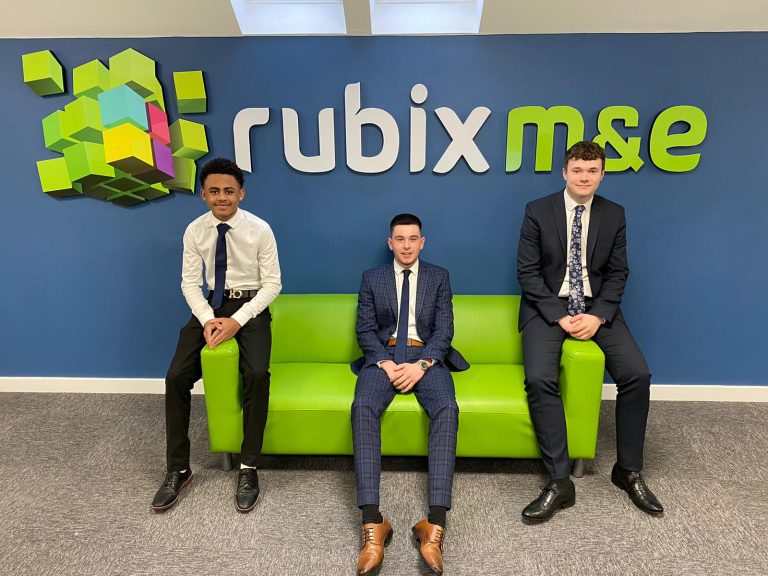 Three young professionals in formal attire sitting and standing in office with Rubix MSE logo.