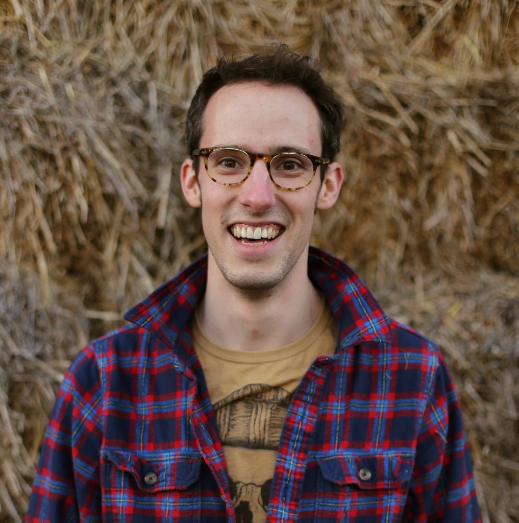 Young man smiling in Suffolk countryside with dry grass background.