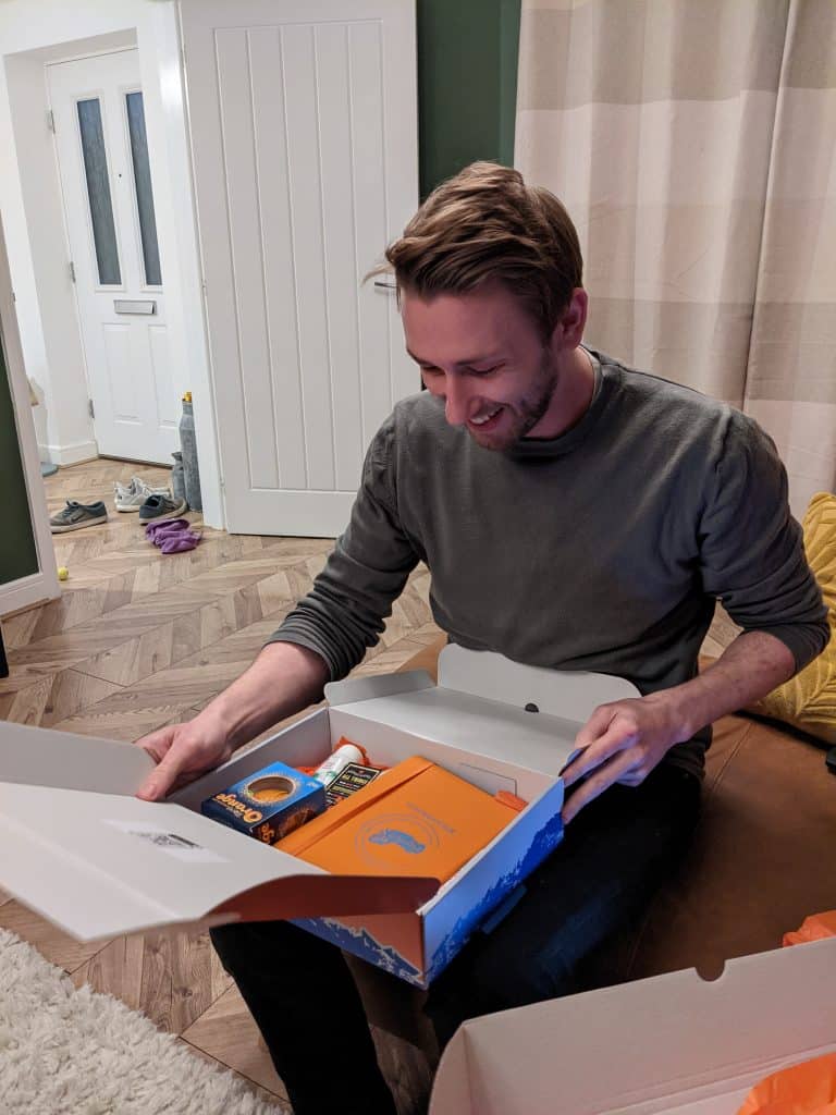 Happy man opening a box of snacks and gifts at home.