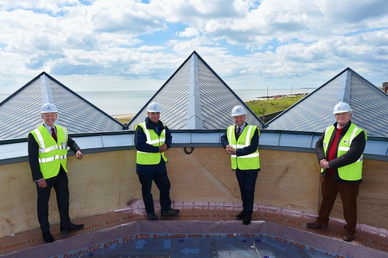 Construction workers inspecting a building roof with a scenic coastal view in Suffolk.