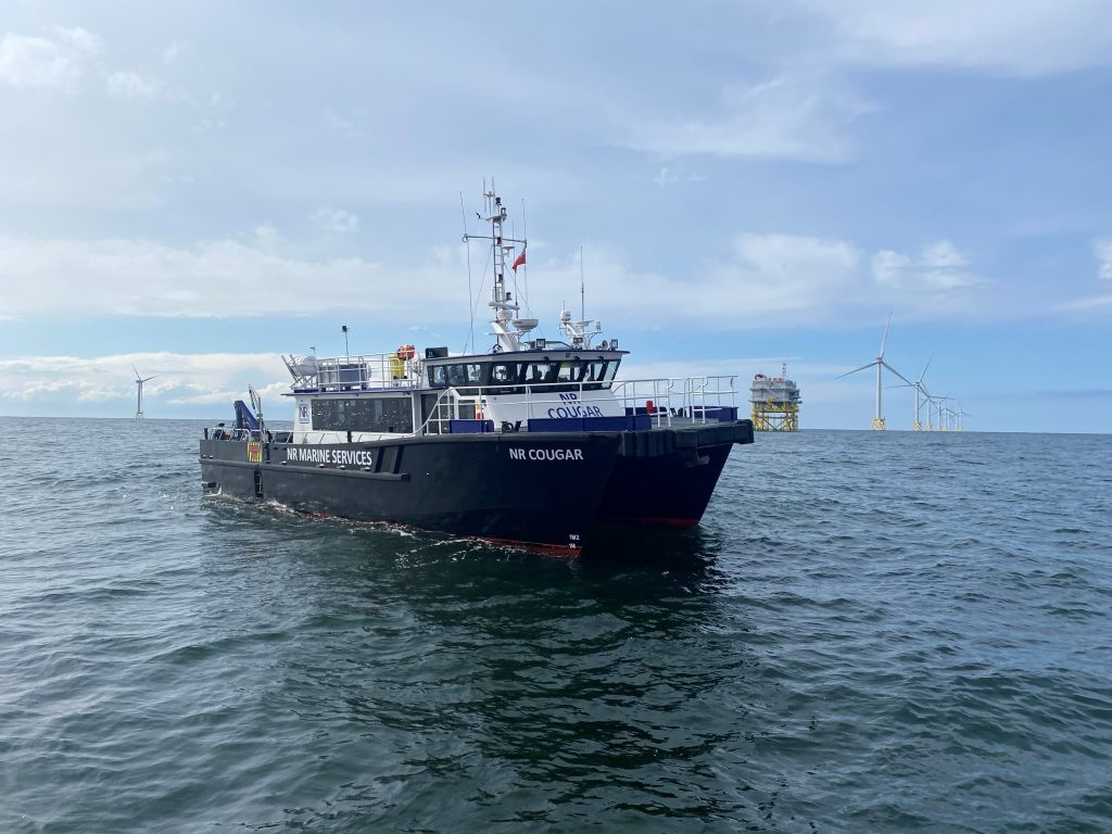 Suffolk marine patrol boat on the sea with wind turbines in the background.