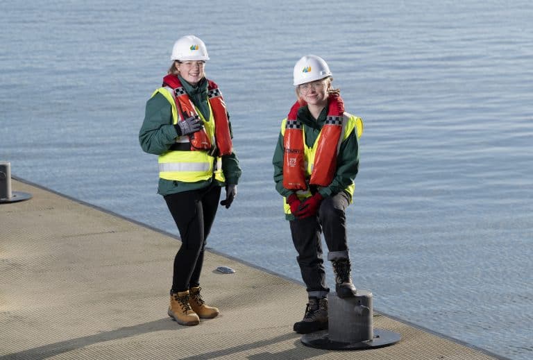 Two workers in safety gear on a dock by the water in Suffolk, demonstrating marine construction expe.