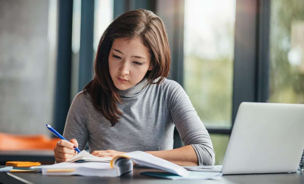 Student studying with laptop and notes in a modern office or library setting.