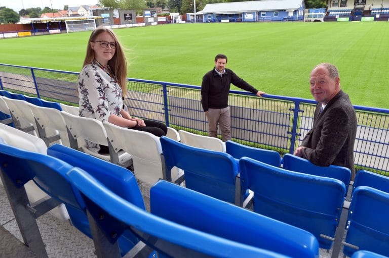 Three people at a Suffolk football stadium, social distancing on the stands.