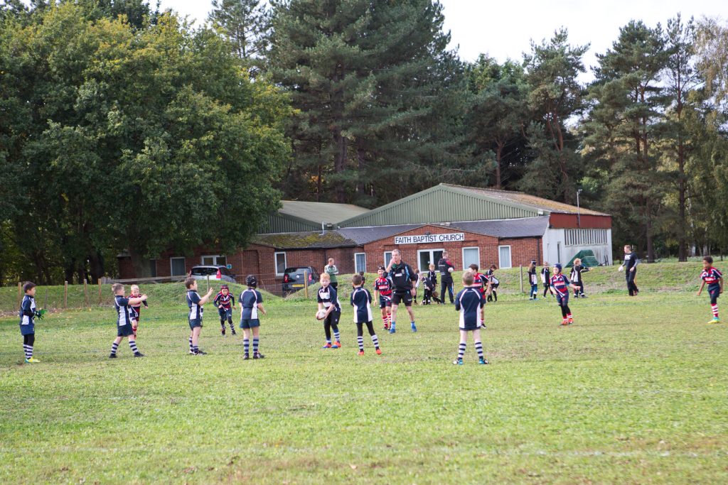Youth football players practicing drills on a grassy field at Suffolk sports club.