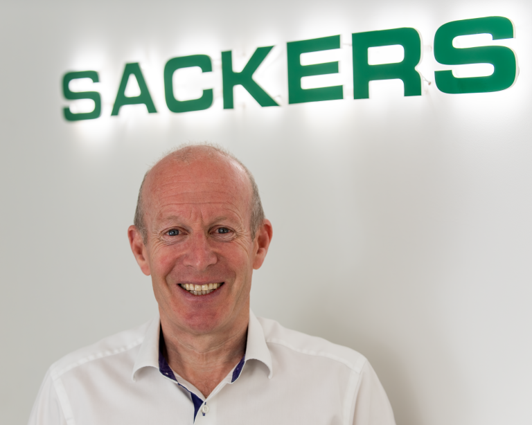 Business professional smiling in front of Suffolk Business sign, promoting local enterprise.