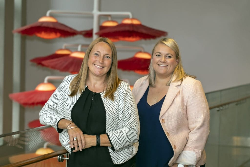 Two professional women smiling at a Suffolk business event, standing near red umbrellas.