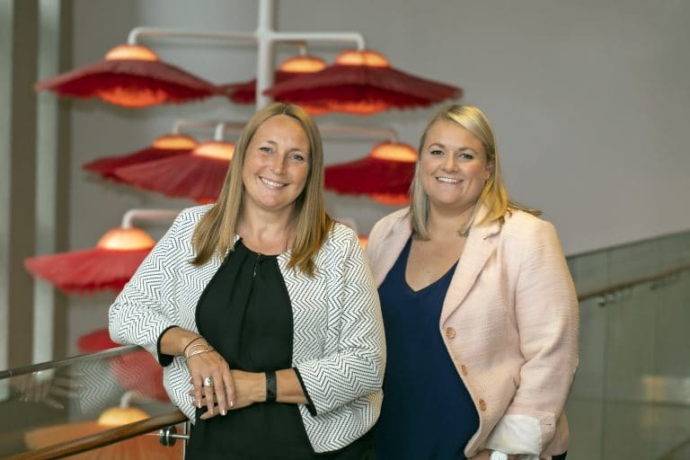 Two professional women smiling at a Suffolk business event, standing near red umbrellas.
