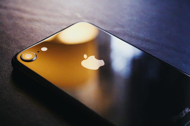 Modern black smartphone with Apple logo on dark surface, close-up.