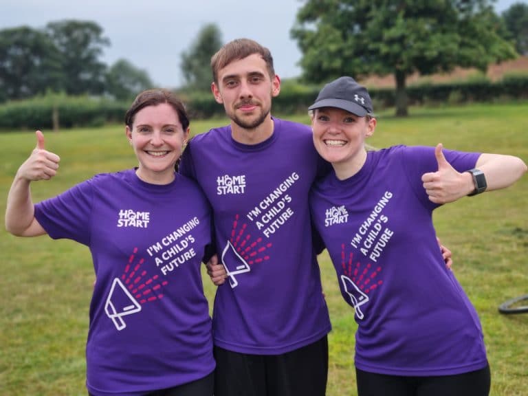 Suffolk Business team members in purple T-shirts outdoors, smiling and giving thumbs up.