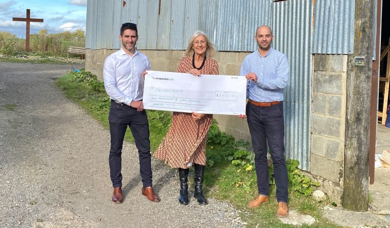Suffolk Business team holding a large cheque outdoors, celebrating success.