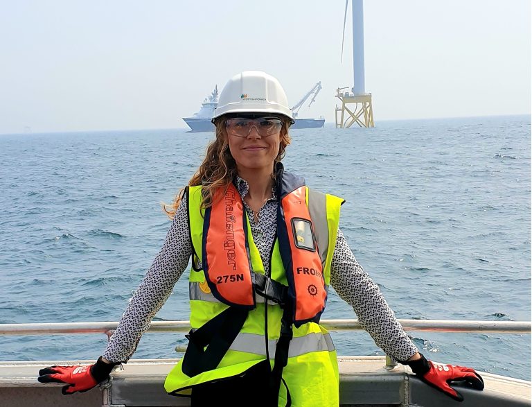 Offshore engineer in Suffolk with safety gear near oil rig and sea.
