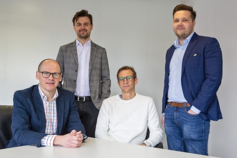 Diverse professional team of four men in formal and casual attire in a modern office setting.