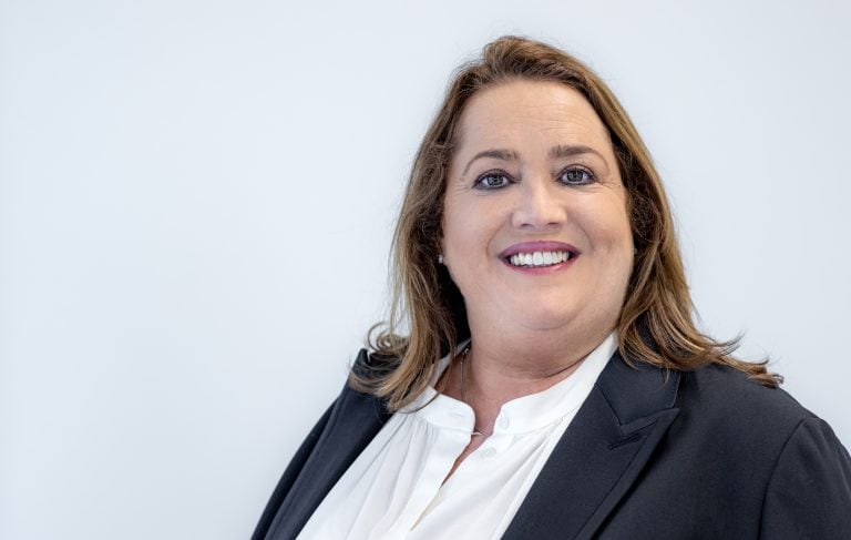 A woman in professional attire smiling against a plain background.